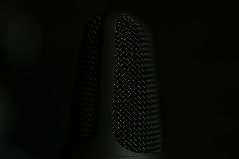 A detailed macro shot of a microphone in a studio setting with a dark background.